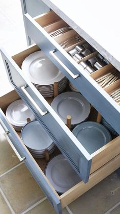 an open drawer with many plates and bowls in it on top of a tile floor