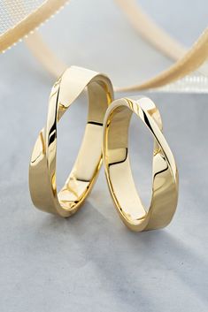 two gold wedding rings sitting next to each other on top of a white table cloth