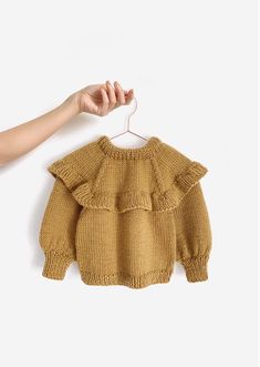 a hand is holding up a sweater with ruffles on it