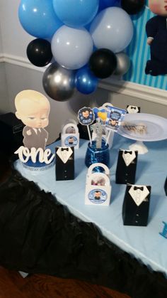 a table topped with blue and black balloons next to a baby's first birthday cake