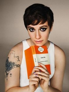 a woman holding an orange and white book in her hands with tattoos on her arm