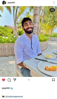 a man sitting at a table with food on it and palm trees in the background