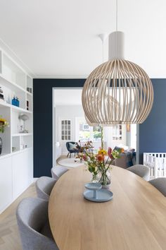 a dining room table with chairs and a vase on top of it in front of a blue wall