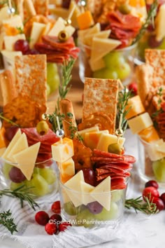 cheese, crackers and grapes are arranged in small glass bowls on a table with other snacks