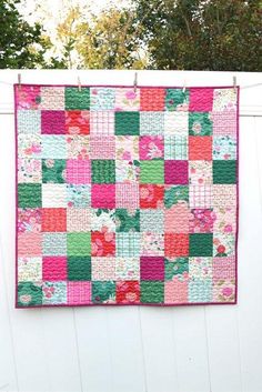 a pink and green patchwork quilt hanging on a white fence