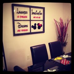 a dining room table with four chairs and mickey mouse signs on the wall above it