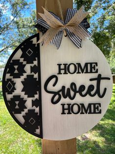 a sign that says home sweet home hanging on a post in the grass with a bow