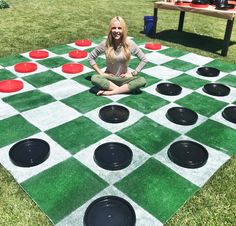 a woman sitting on top of a giant checkered board game in the grass with red and black circles