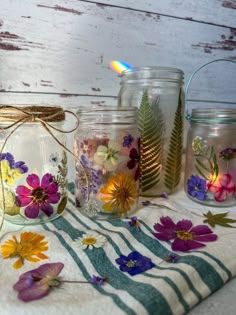 four jars with flowers painted on them are sitting on a striped towel next to a lit candle