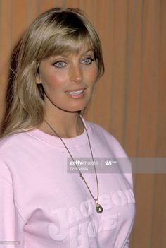 a woman with blonde hair wearing a pink shirt and necklace, posing for the camera