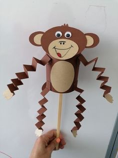 a hand holding up a paper monkey on a stick with eyes and tail, made out of cardboard