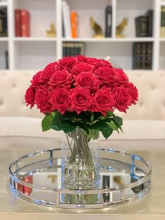 a glass vase filled with red roses on top of a table next to a couch