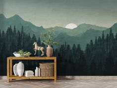 a table with vases on it in front of a wall mural that has mountains and trees