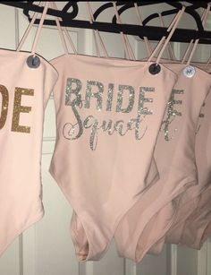 three pink onesuits hanging from a rack with bride and groom written on them