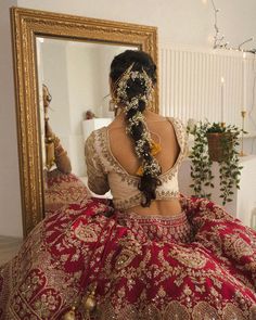 a woman in a red and gold bridal gown looking at herself in the mirror