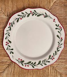 an empty white plate with red trim and green leaves on it sitting on a wicker surface