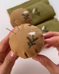 two hands are holding an object made out of fabric with flowers and leaves on it