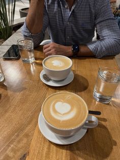 a man sitting at a wooden table with two cups of coffee in front of him