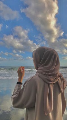 a woman standing on top of a beach next to the ocean under a cloudy sky