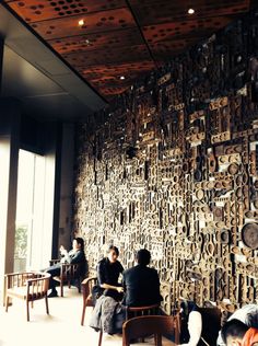 people are sitting at tables in front of a wall covered with wooden carvings and clocks