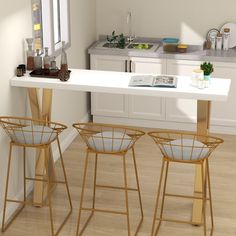 three stools and a table in a room with white walls, wood floors and cabinets