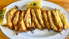 fried fish on a white plate with lemon wedges