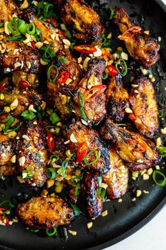 a black plate topped with chicken wings covered in sesame seeds and garnishes