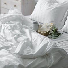 an unmade bed with white sheets, pillows and a book on the end table