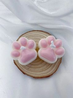 two pink dog paw shaped cookies sitting on top of a piece of wood with white frosting