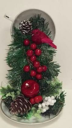 a red bird sitting on top of a christmas tree next to pine cones and berries