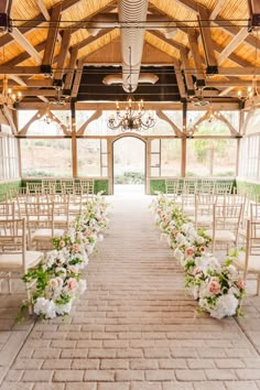 an indoor wedding venue with white chairs and floral arrangements on the aisle leading up to the ceremony room