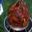 a large roasting turkey is being cooked on the grill with someone's feet standing next to it