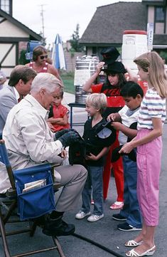 an older man sitting in a chair with children around him and other people standing behind him