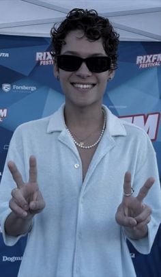 a woman in white shirt and sunglasses giving the peace sign with both hands at an event