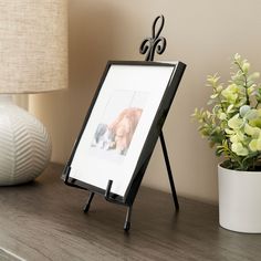 an easel with a picture on it next to a lamp and potted plant