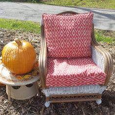 an orange pumpkin sitting on top of a wooden chair next to a white and red cushion