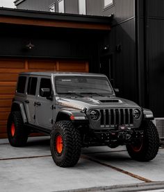 a gray jeep parked in front of a garage with red lights on the tires and rims