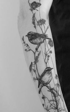 a black and white photo of some birds on a branch with flowers in the background