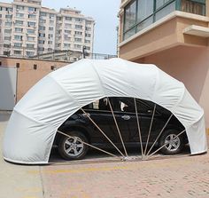 a black car parked under a white tent in front of a tall building with balconies