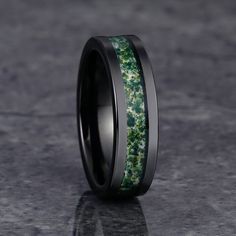 a wedding band with green moss inlays and black beveled edges is shown