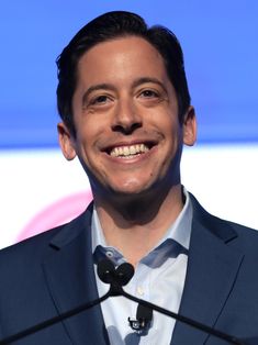 a man in a suit and tie smiles at the camera while standing behind a microphone