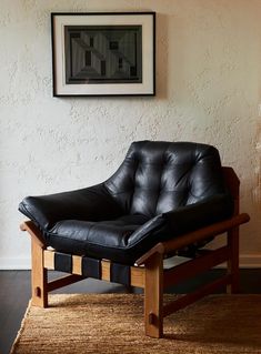 a black leather chair sitting on top of a rug in front of a white wall