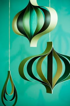 three paper ornaments hanging from strings against a blue wall with green and black designs on it