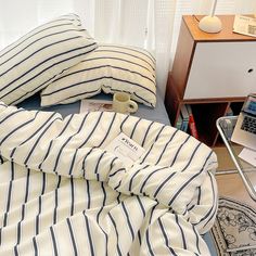 there is a bed with blue and white striped sheets on it, next to a laptop