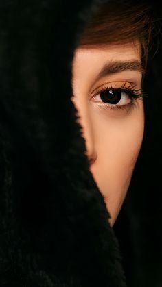 a woman's eye is seen through the hood of a black fur - lined coat