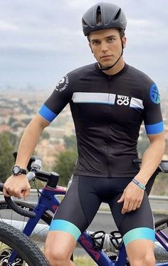 a man sitting on top of a bike next to a blue bicycle with the city in the background