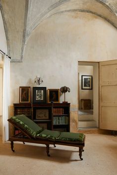 a green chaise lounge sitting in the middle of a room next to bookshelves