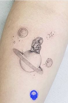 a small tattoo on the arm of a person with an astronaut and planets in the background