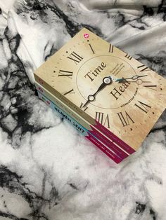 two books sitting on top of each other next to a marble table with a clock