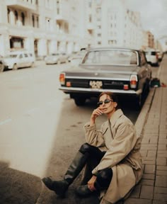 a woman sitting on the side of a road next to a car and wearing black boots